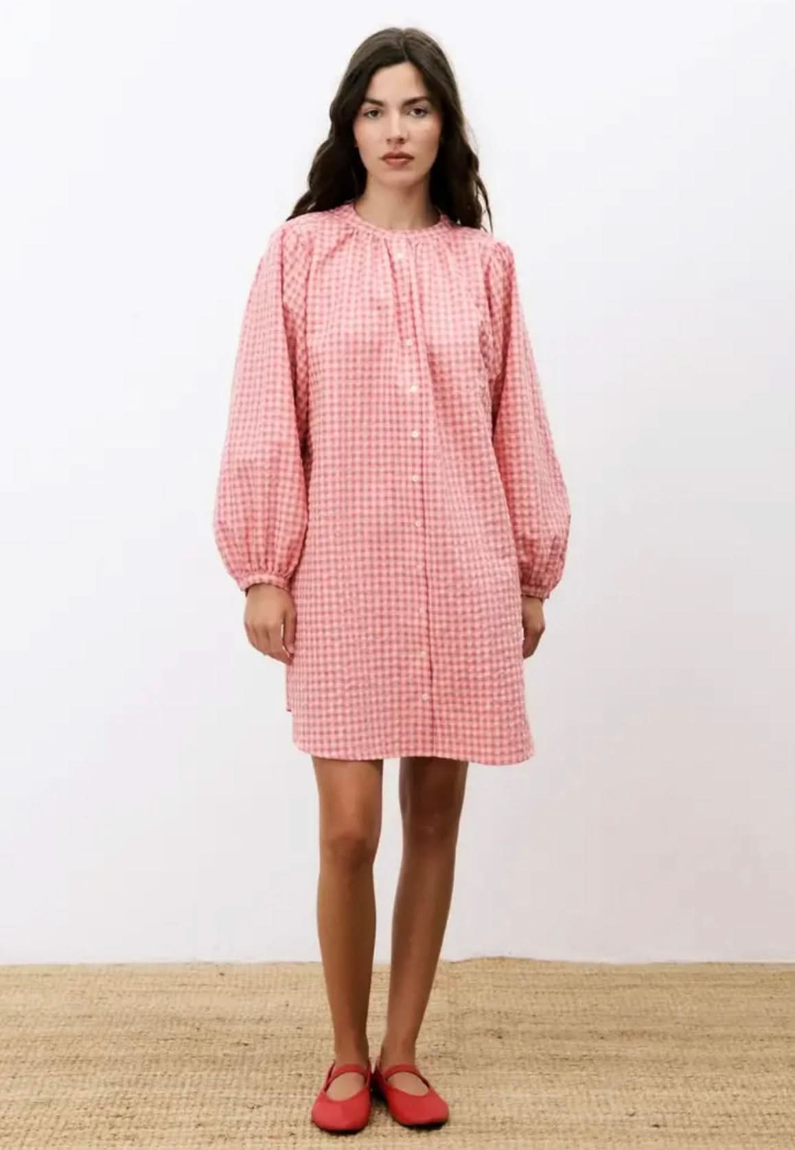 Woman wearing a pink checkered dress with long sleeves on a white background