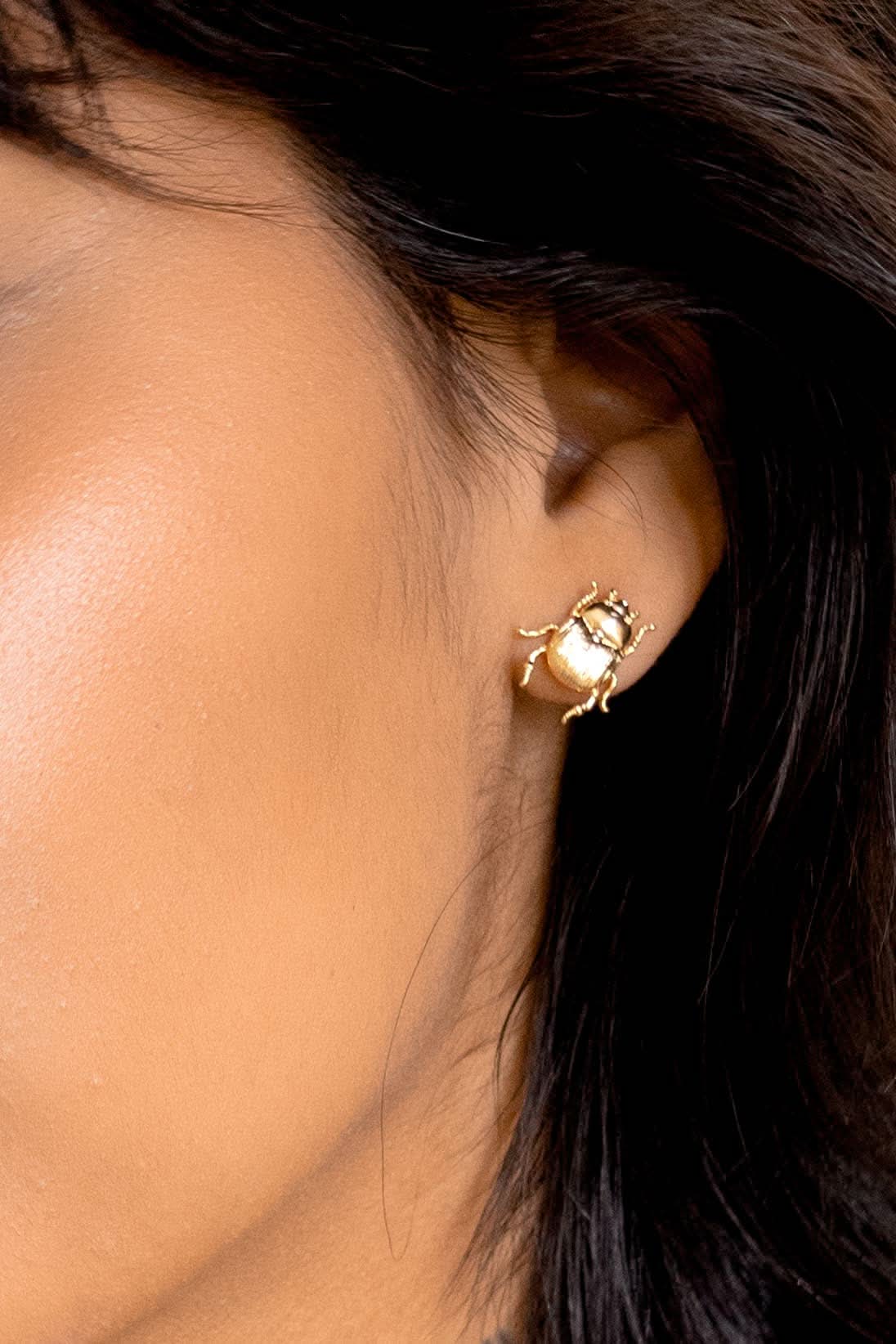 Close-up of a person wearing a gold earring with a gemstone.