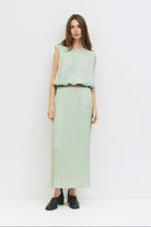 Woman standing against a white wall wearing matching sea foam, Sage green textured skirt and blouse