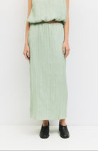 Woman standing against a white wall wearing matching sea foam, Sage green textured skirt and blouse