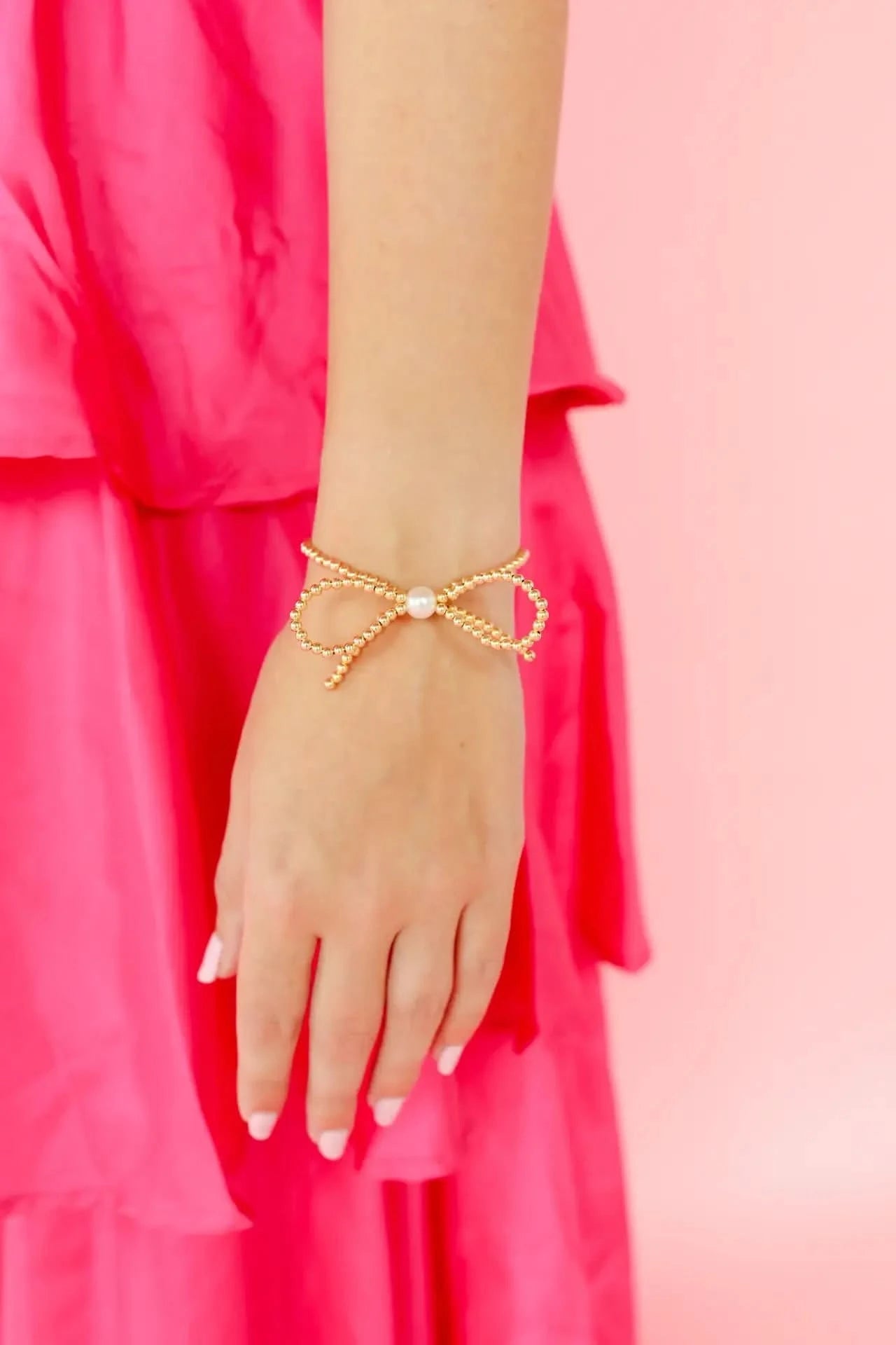 Gold bracelet with a pearl on a hand against a pink background