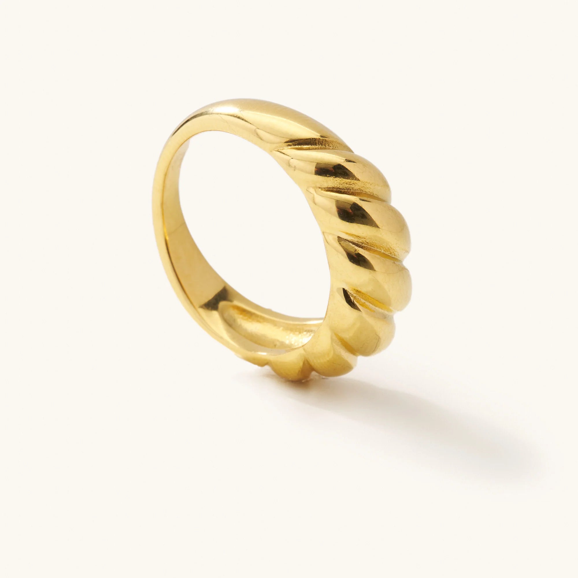 Gold ring with a twisted croissant design standing upright on a white background