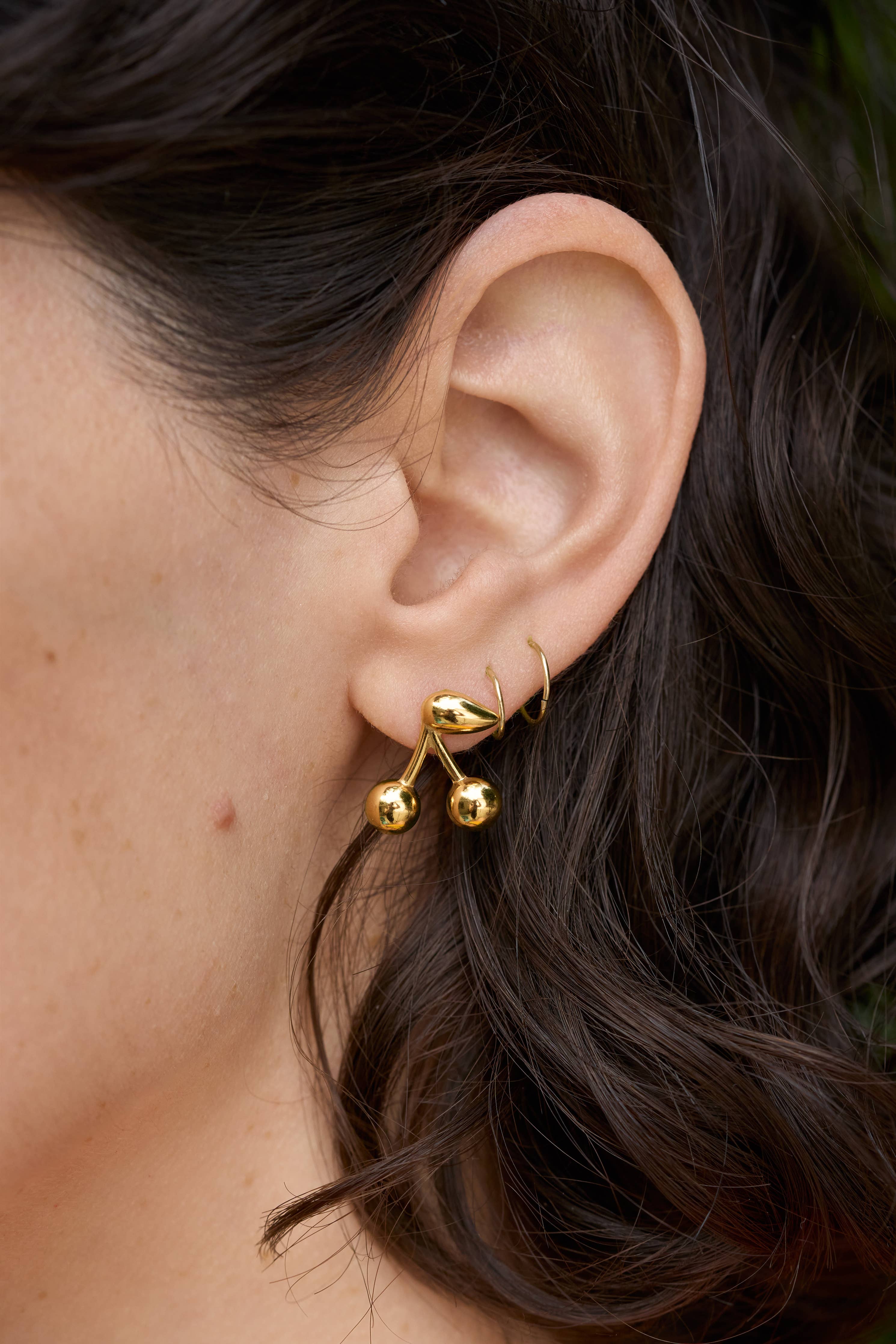 Gold Maraschino Studs Close-up of an ear wearing a gold earring with dark hair.