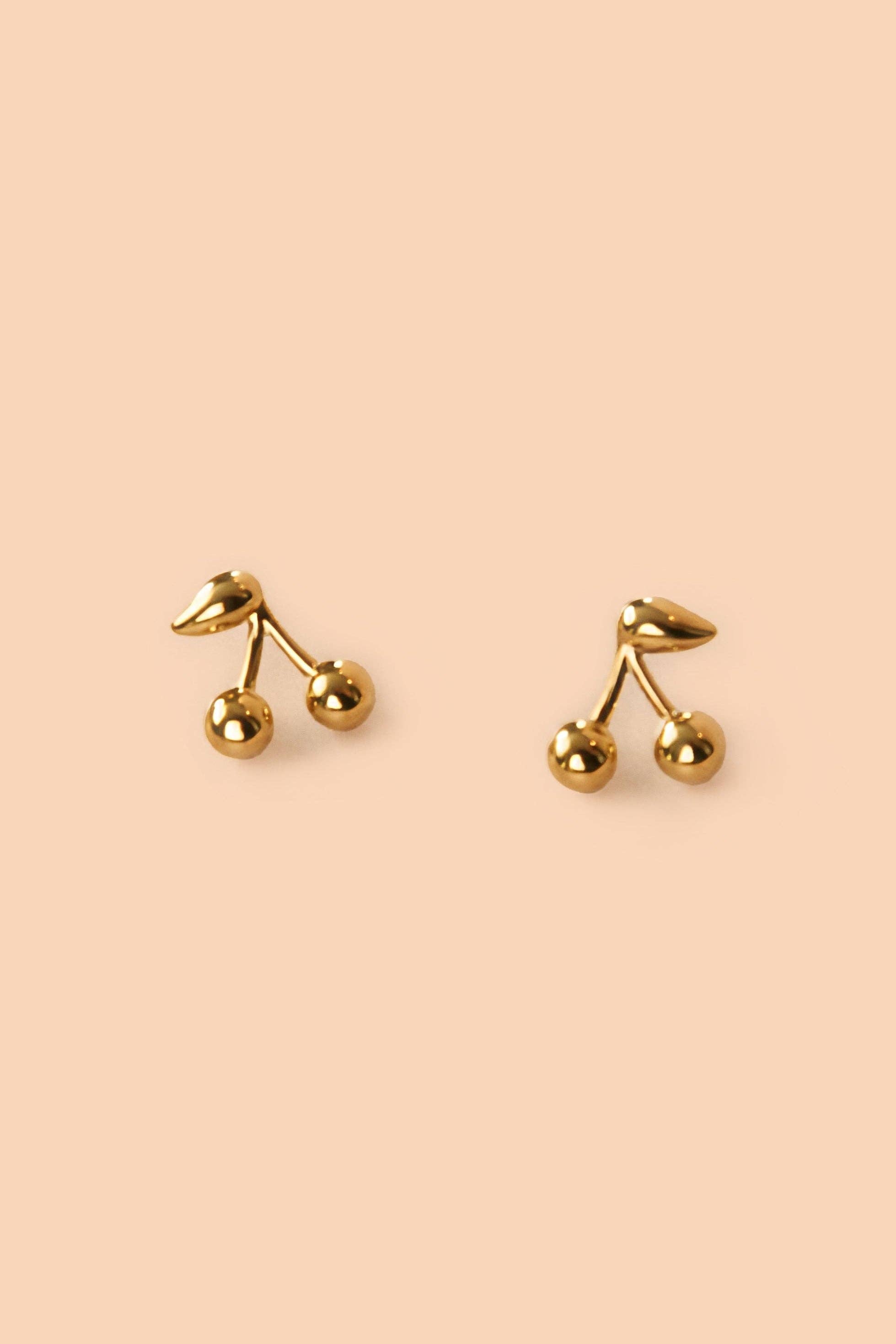 Maraschino Studs Gold cherry-shaped earrings on a beige background