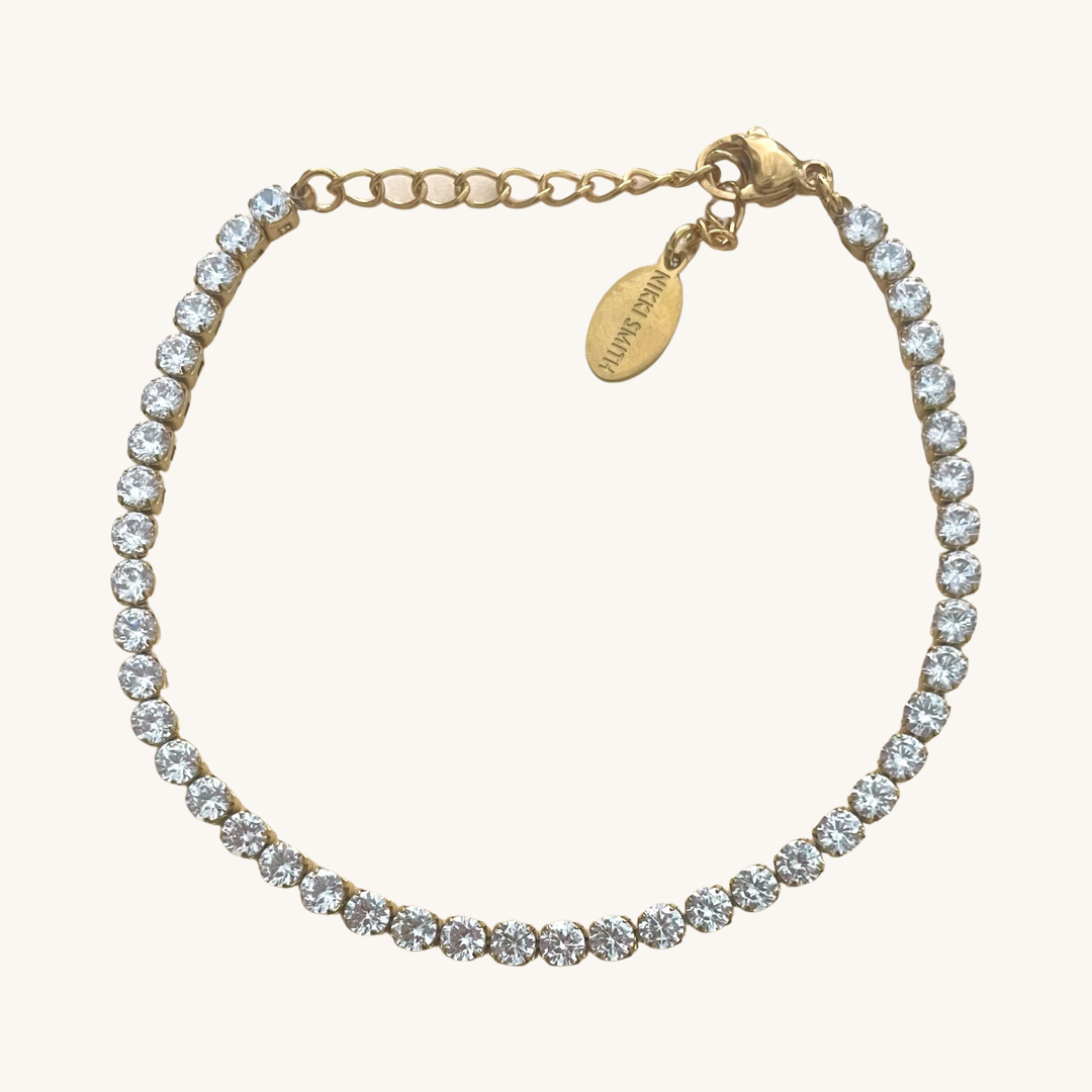 Dainty gold shimmer tennis bracelet laying on a white background 