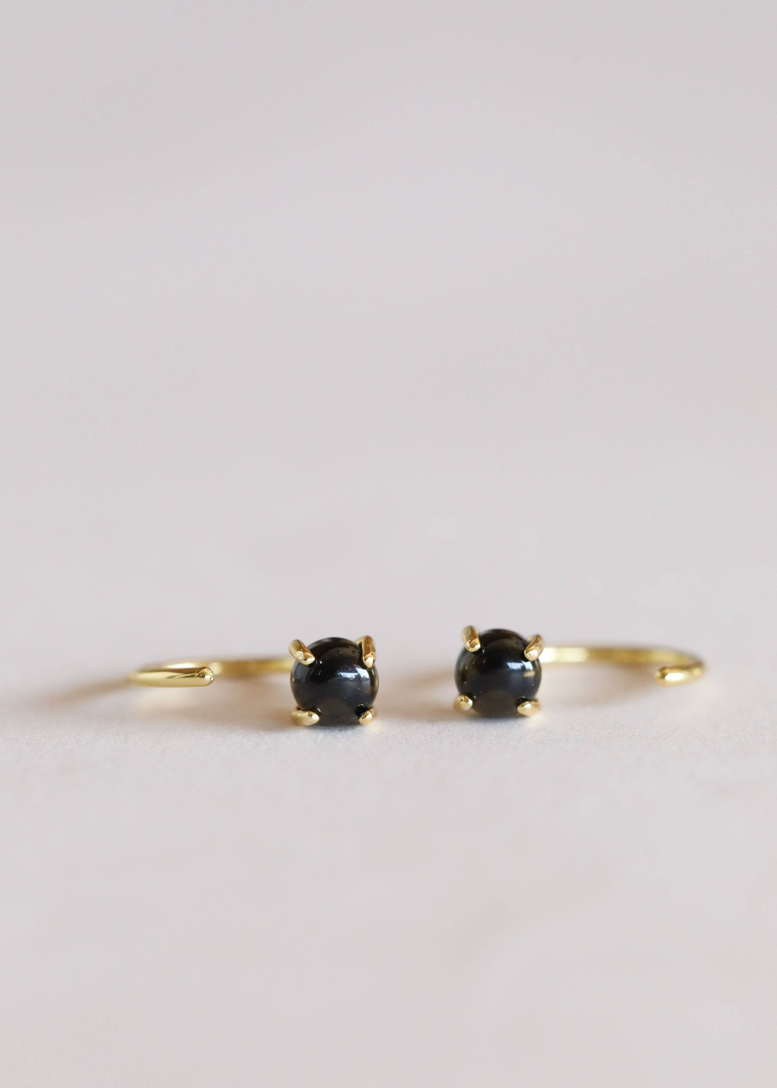 Pair of gold hoop earrings with black gemstones on a light gray background