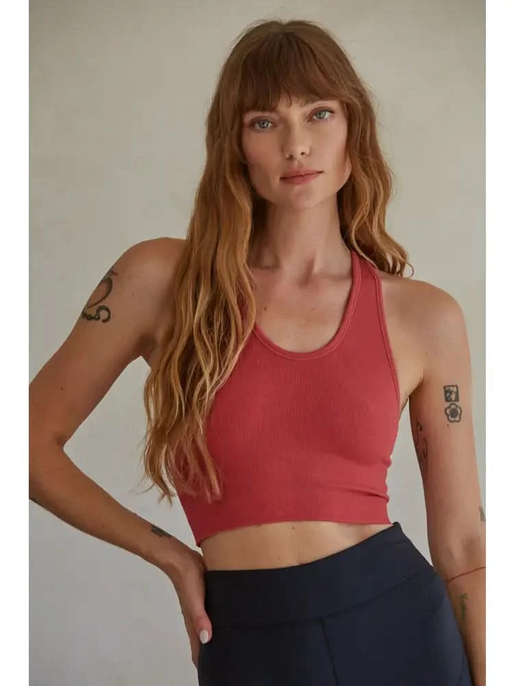 Woman wearing a red knit seamless ribbed scoop with a U-V neckline tank top with black pants standing in front of a blank background. 