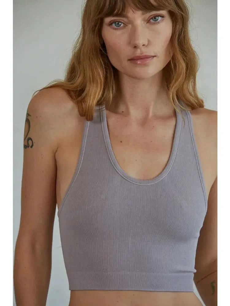 Woman wearing a mauve knit seamless ribbed scoop with a U-V neckline tank top standing in front of a blank background. 