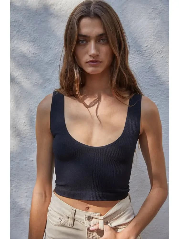 Woman wearing a black knit seamless chevron design with a sleeveless U-V neckline tank top behind a white wall. 