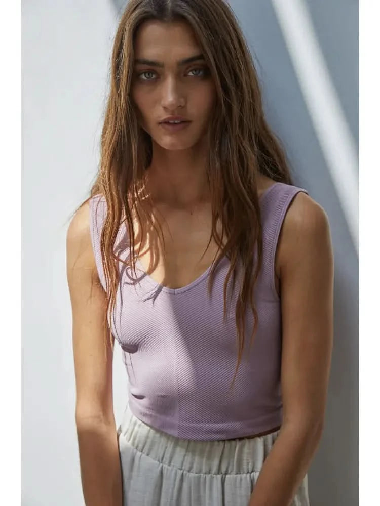 Woman wearing a purple knit seamless chevron design with a sleeveless U-V neckline tank top behind a white wall. 