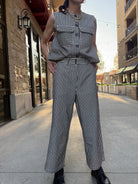 Woman standing outside wearing Striped denim and cream vintage vest, full button up, with big pockets in front. And wearing the matching pants