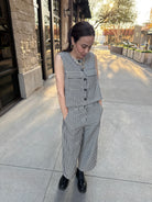 Woman standing outside wearing Striped denim and cream vintage vest, full button up, with big pockets in front. and wearing the matching pants 