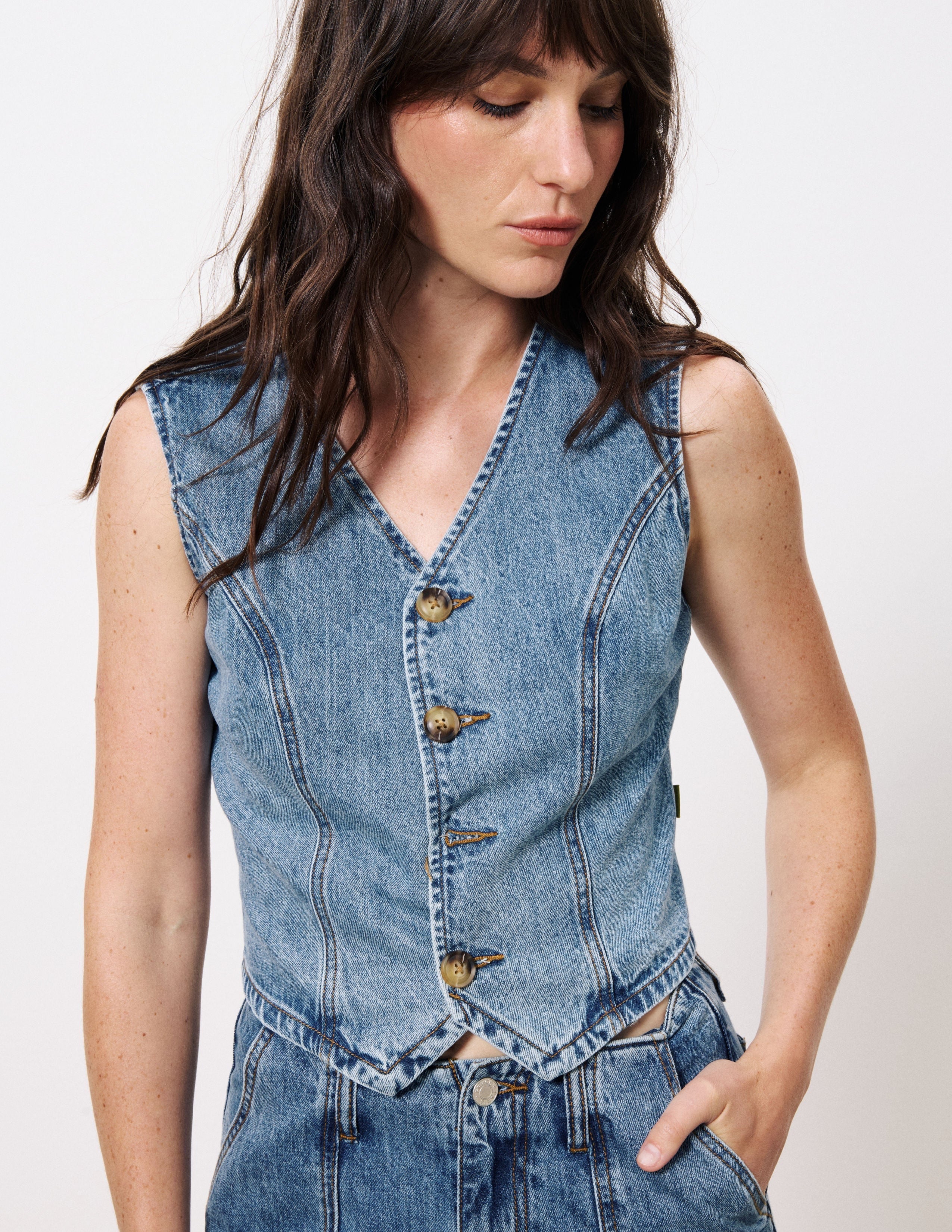 Woman standing against white background wearing blue jean button up vest