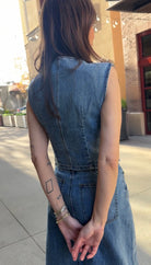 Woman standing outside, facing away from the camera wearing blue jean button up vest