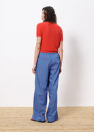 Woman with back facing viewer wearing red knit style sweater cardigan and blue striped drawstring pants 