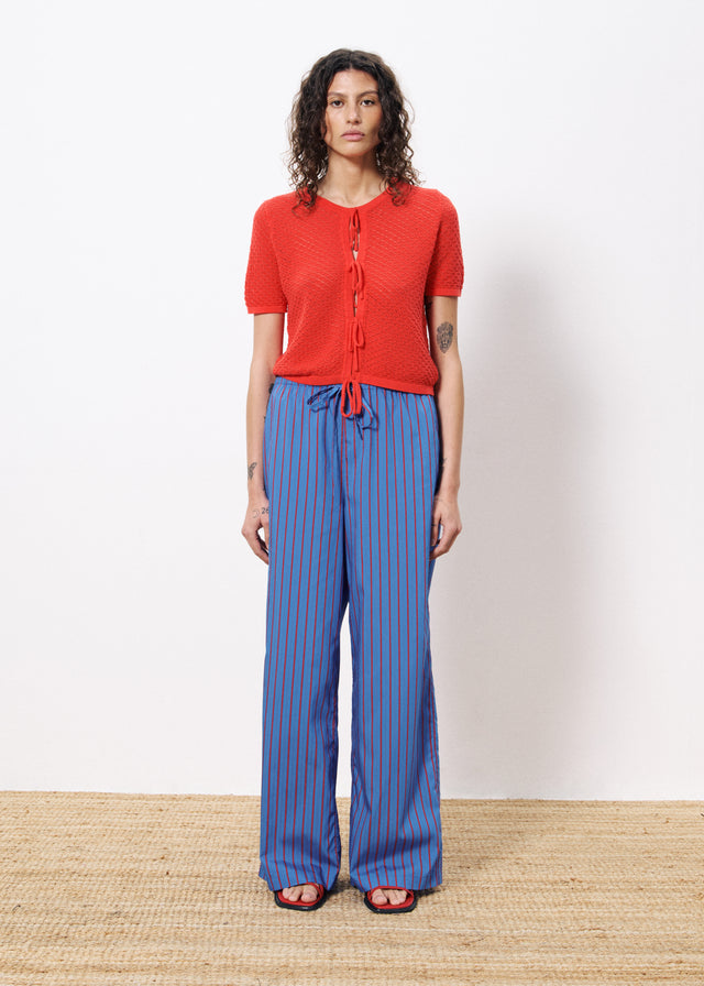 Woman wearing red knit style sweater cardigan with three adjustable string ties in the front and blue striped drawstring pants 