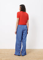 Woman facing away wearing red top and blue pants with red vertical stripes all over 