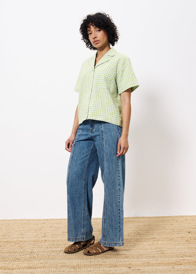 Woman wearing yellow green and white gingham button up cropped blouse with front pocket paired with wide leg blue jeans