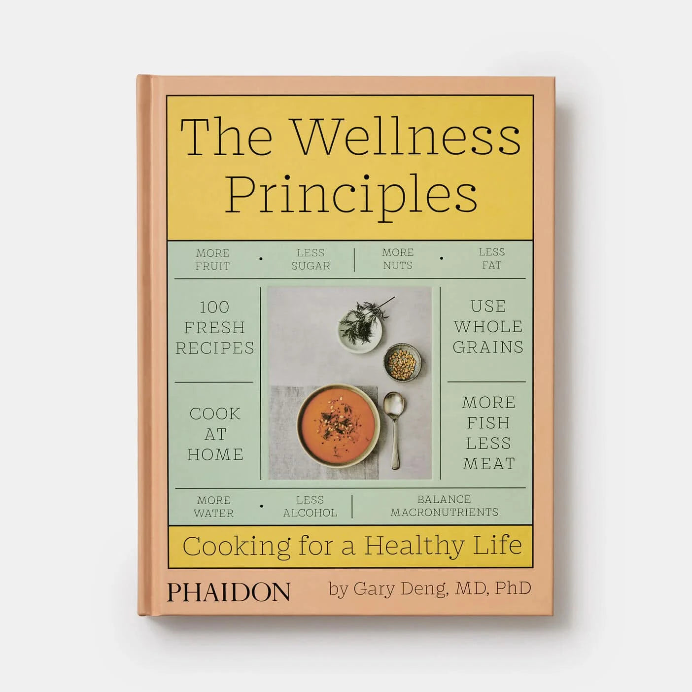 Pink orange book with yellow and turquoise highlights. “the wellness principles- cooking for a healthy life” written in black with photo of white bowl of tomato soup, a spoon, small gray bowl of pine nuts, and white plate with dill