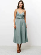 Woman wearing green vertically striped sleeveless, long silhouette dress with a distinctive V-neckline, slender shoulder straps, and a tie in the back