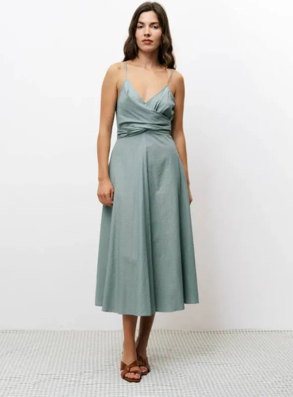 Woman wearing green vertically striped sleeveless, long silhouette dress with a distinctive V-neckline, slender shoulder straps, and a tie in the back