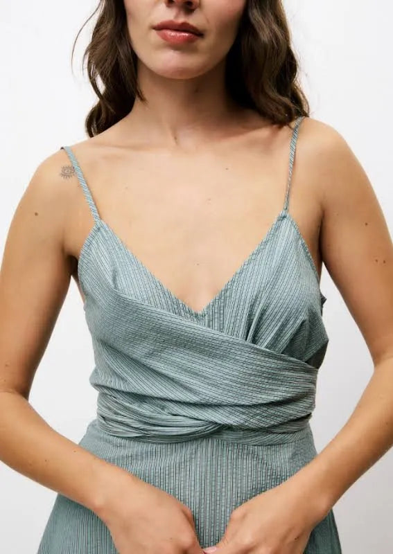Woman wearing green vertically striped sleeveless, long silhouette dress with a distinctive V-neckline, slender shoulder straps, and a tie in the back