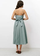 Woman wearing green vertically striped sleeveless, long silhouette dress with a distinctive V-neckline, slender shoulder straps, and a tie in the back