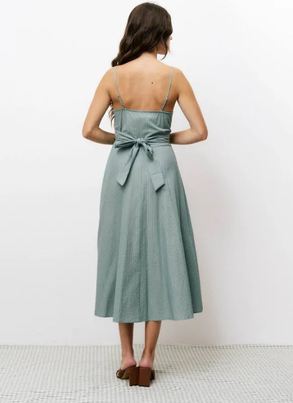 Woman wearing green vertically striped sleeveless, long silhouette dress with a distinctive V-neckline, slender shoulder straps, and a tie in the back