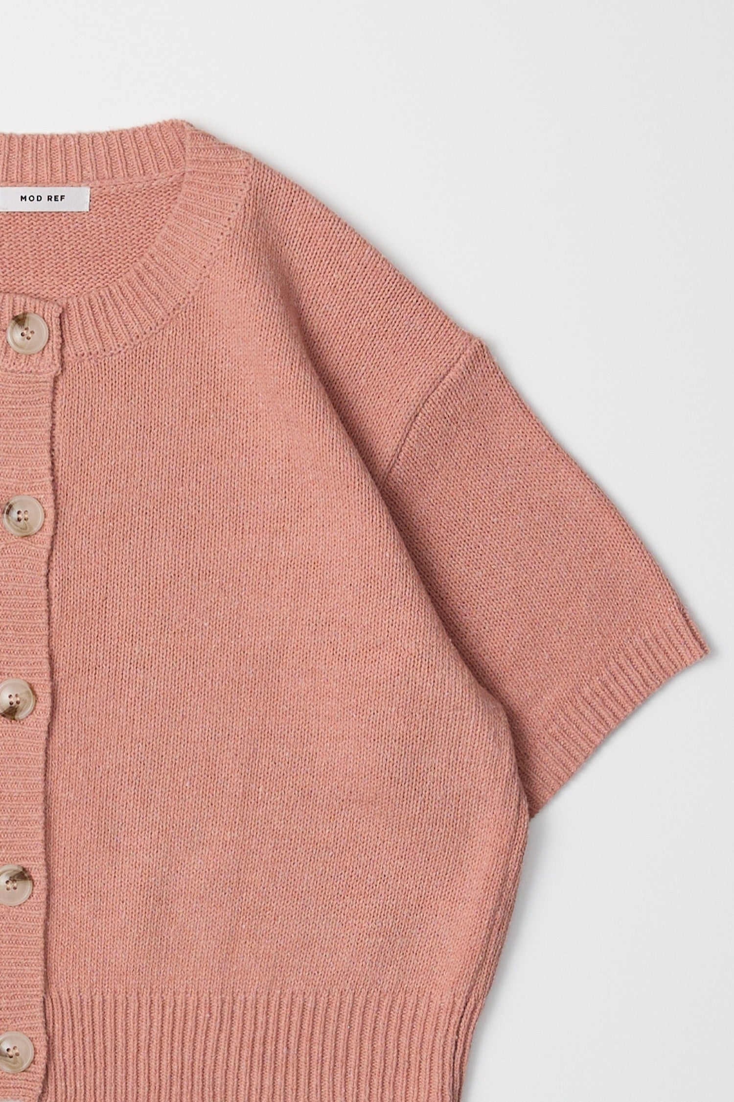 Close up detail of a salmon pink, short sleeved, sweater cardigan 