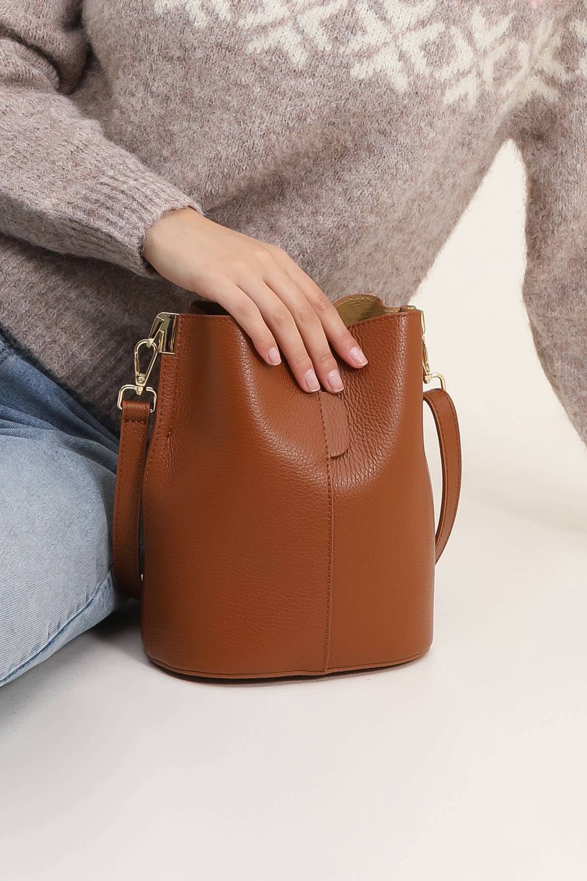 Brown leather handbag held by a person wearing a patterned sweater and jeans on a light background