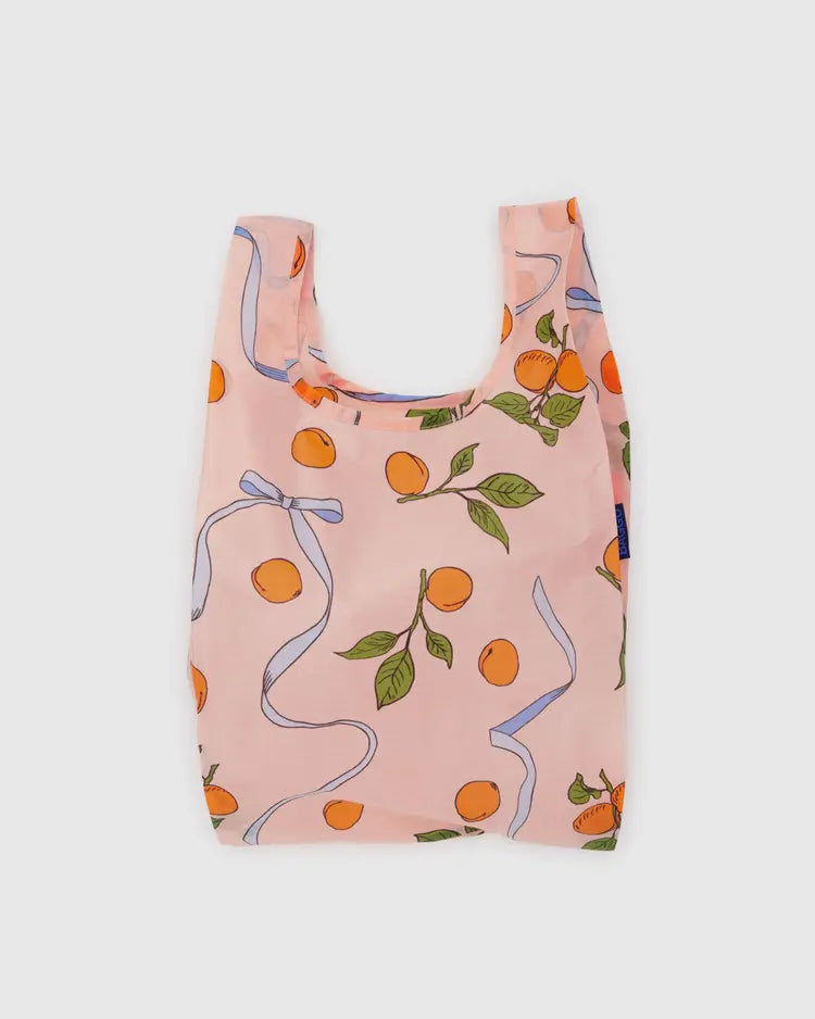 Light pink small reuseable bag with orange apricots and blue ribbons behind a white background. 