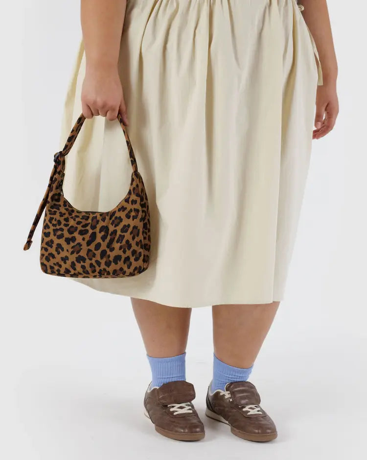 Woman wearing a yellow skirt holding a small over the shoulder leopard purse in hand behind a white background. 