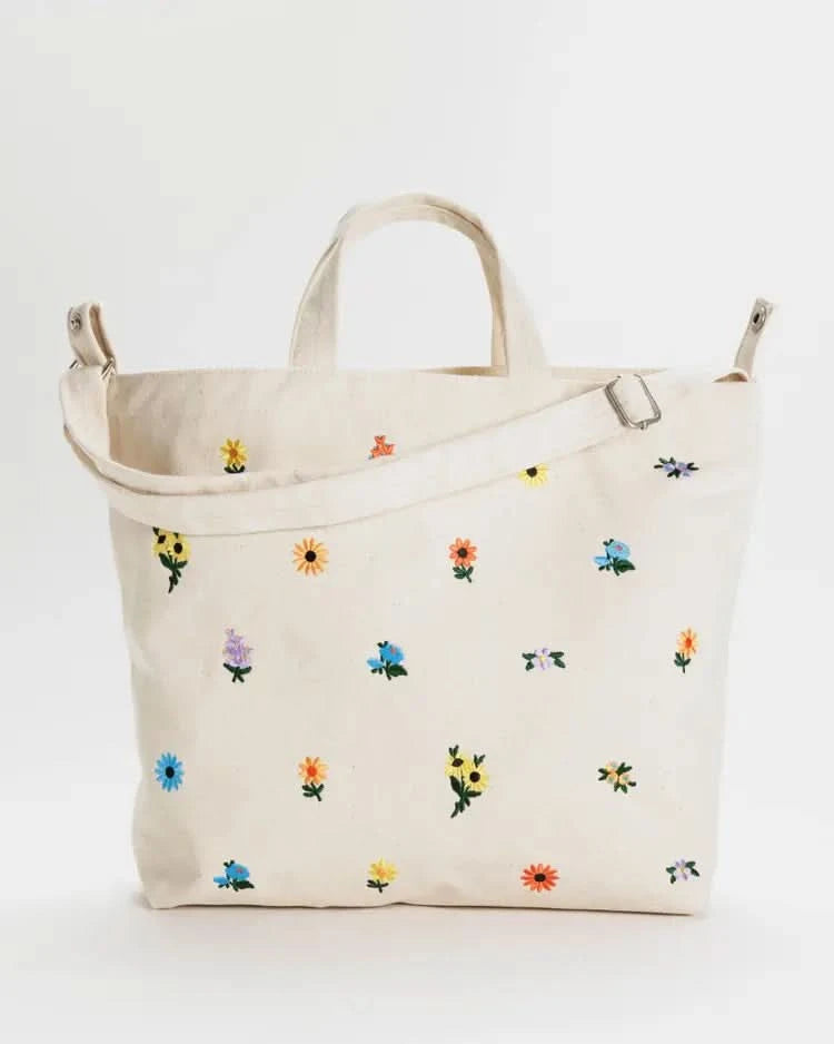 White over the shoulder tote bag with flowers behind a white background. 