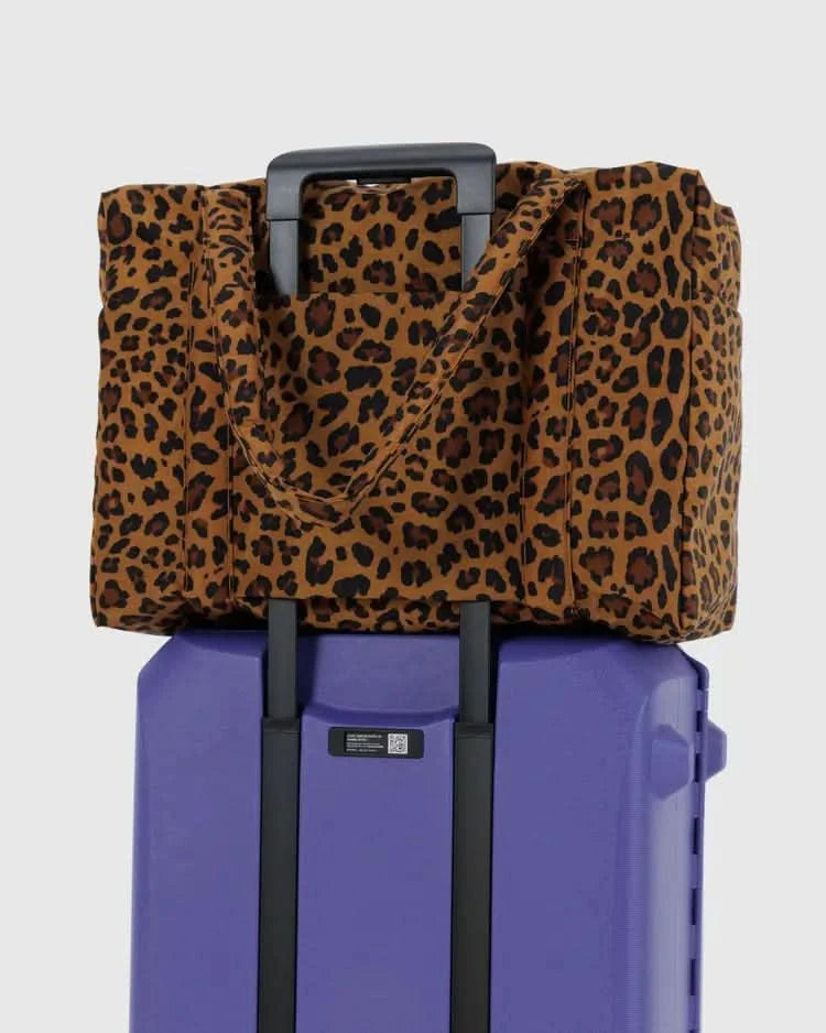 Large leopard over the shoulder carry-on tote bag on a purple suitcase behind a white background. 