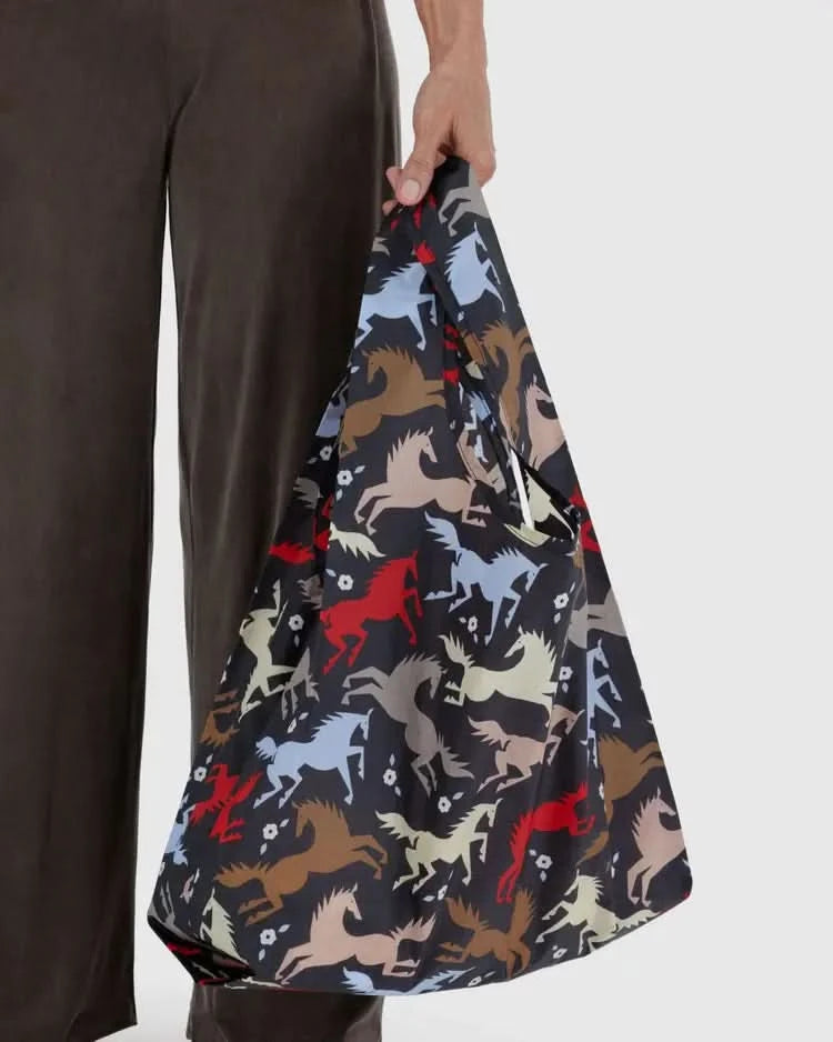 Someone carrying Dark grey black baby baggu reuseable bag with colorful horse cutouts throughout the print 