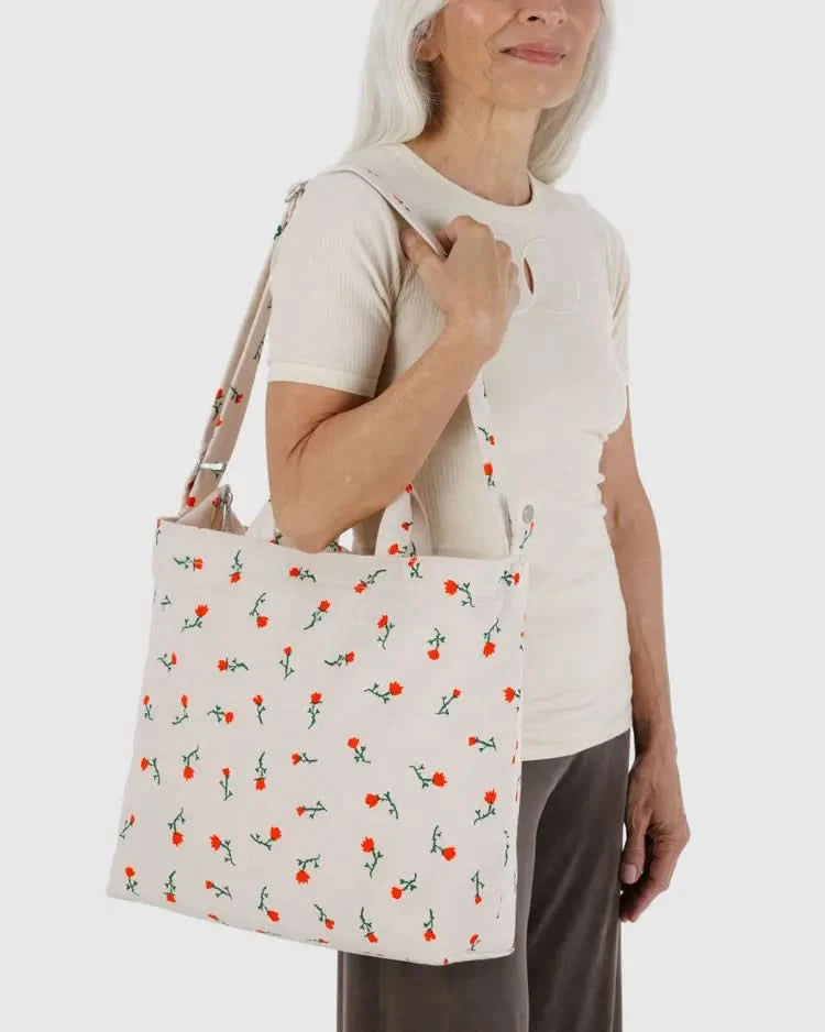 Woman carrying Cream white tote bag with two handle options with embroidered red and green floral designs 