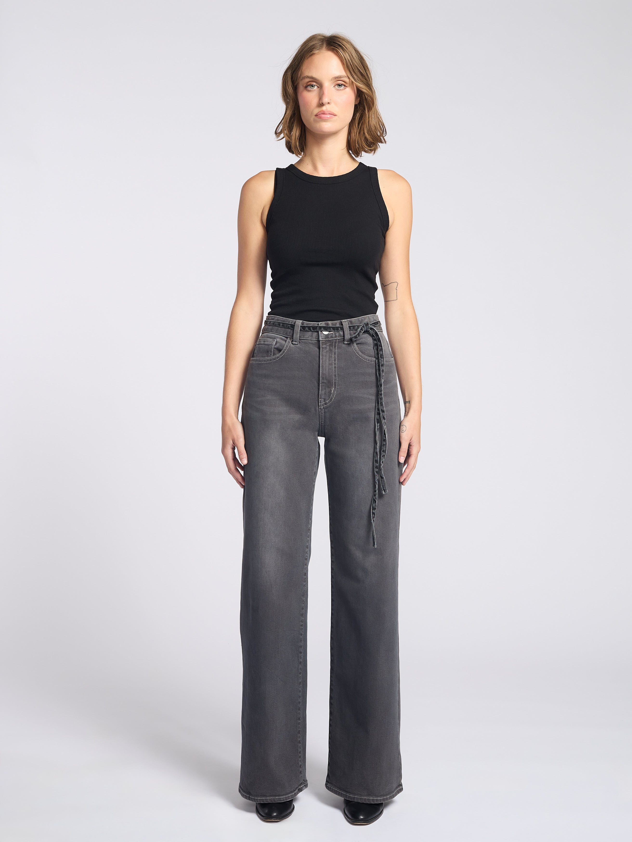 Woman wearing dark grey jeans with string tie belt and black tank top