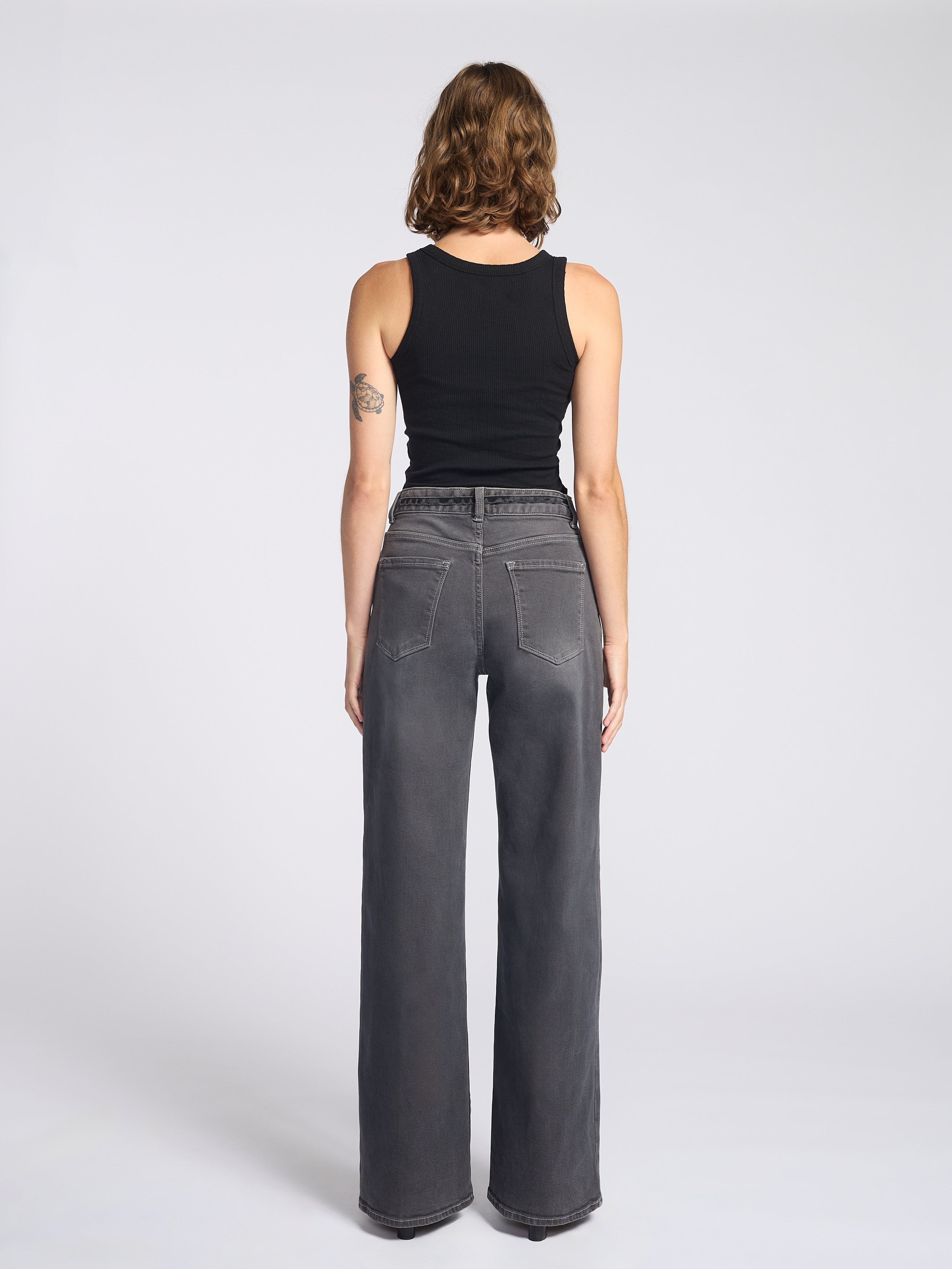 Woman wearing dark grey jeans with string tie belt and black tank top