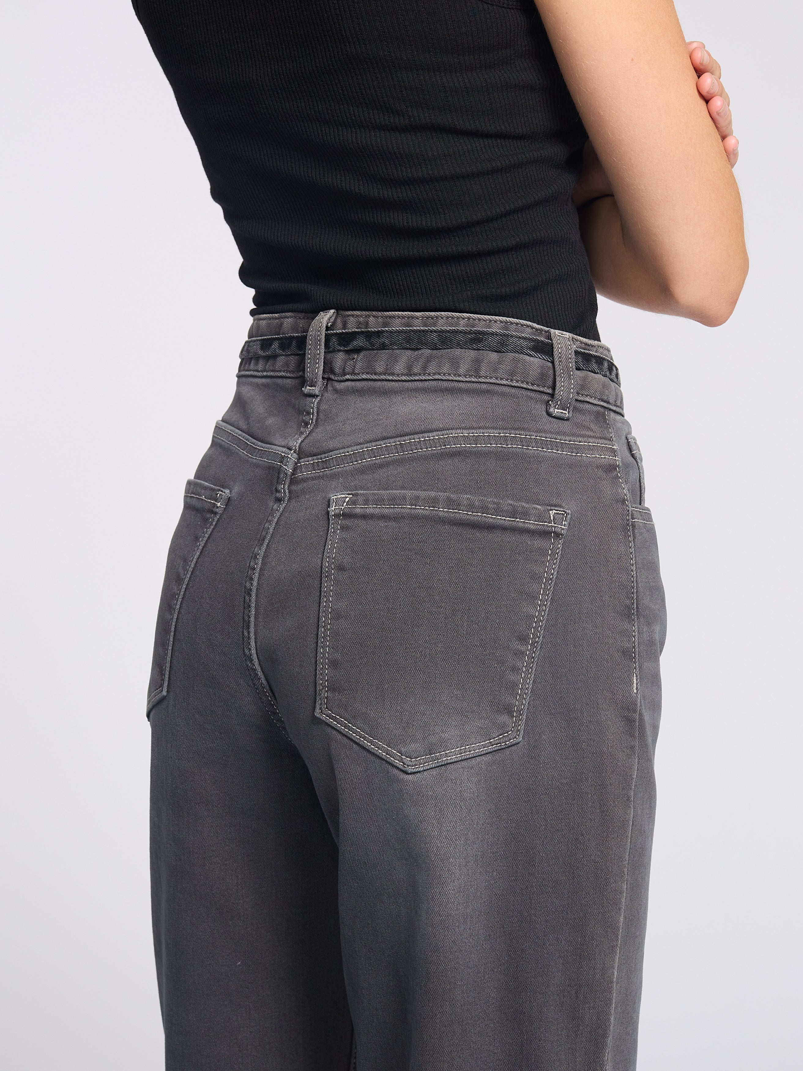 Woman wearing dark grey jeans with string tie belt and black tank top