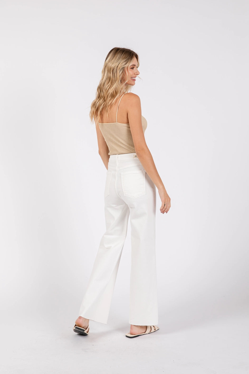 Woman wearing a beige top and white pants on a white background