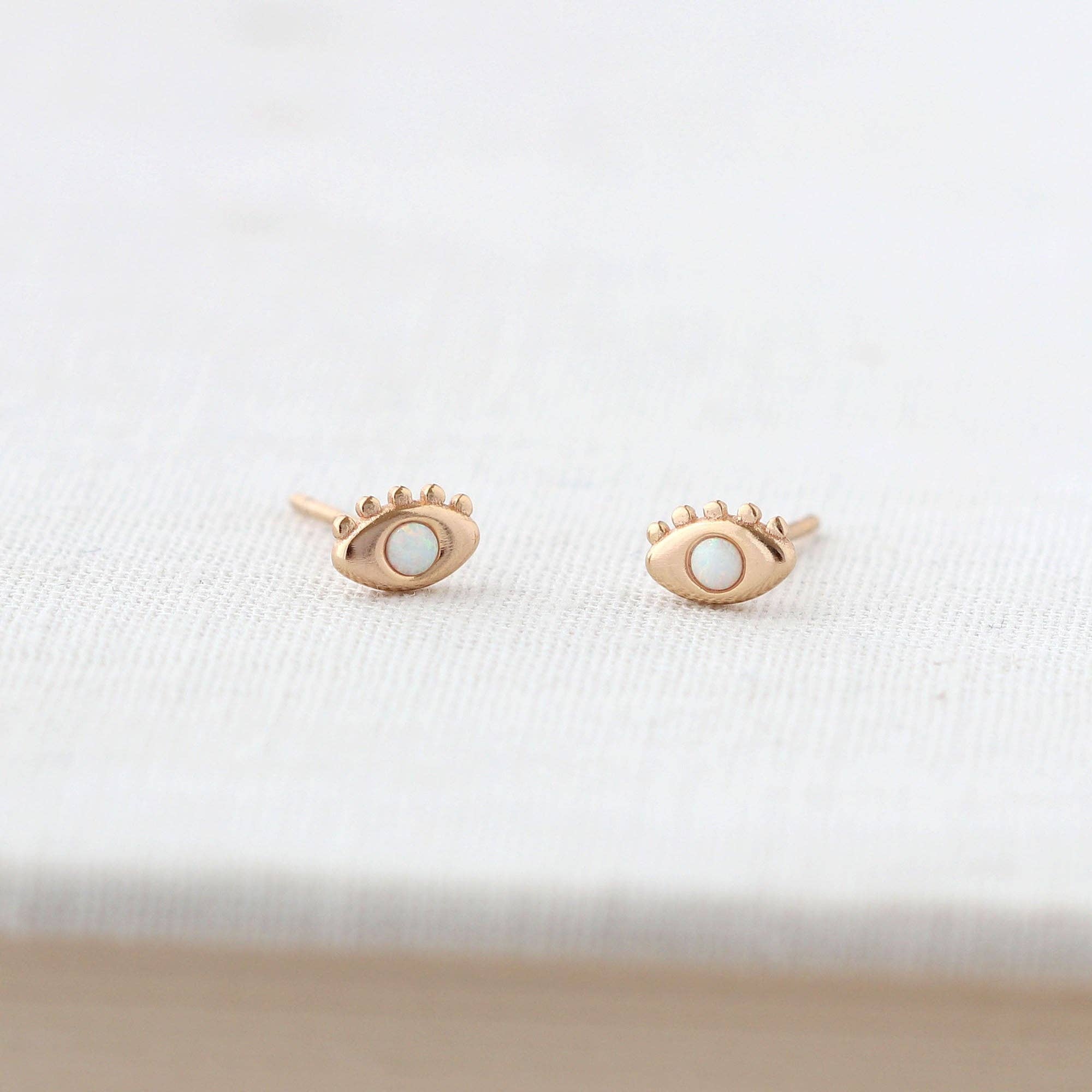 Rose gold eye-shaped earrings on a white fabric background