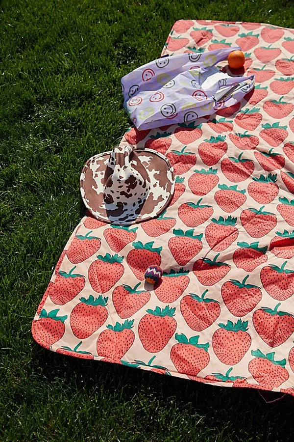 Strawberry-patterned blanket with a hat and folded clothes on grass