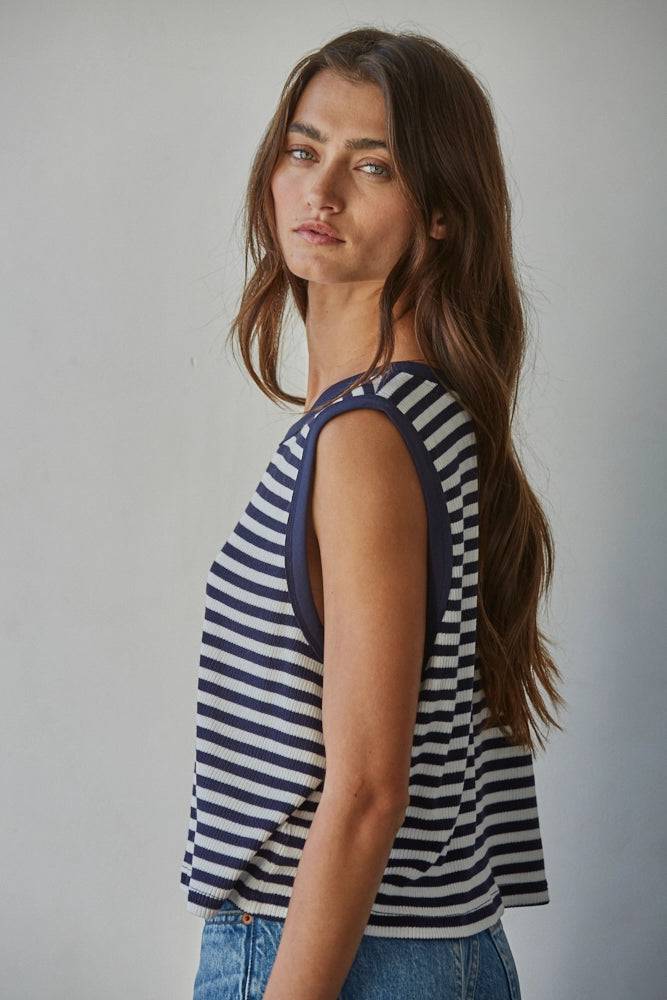 Woman wearing a striped tank top and jeans against a plain background