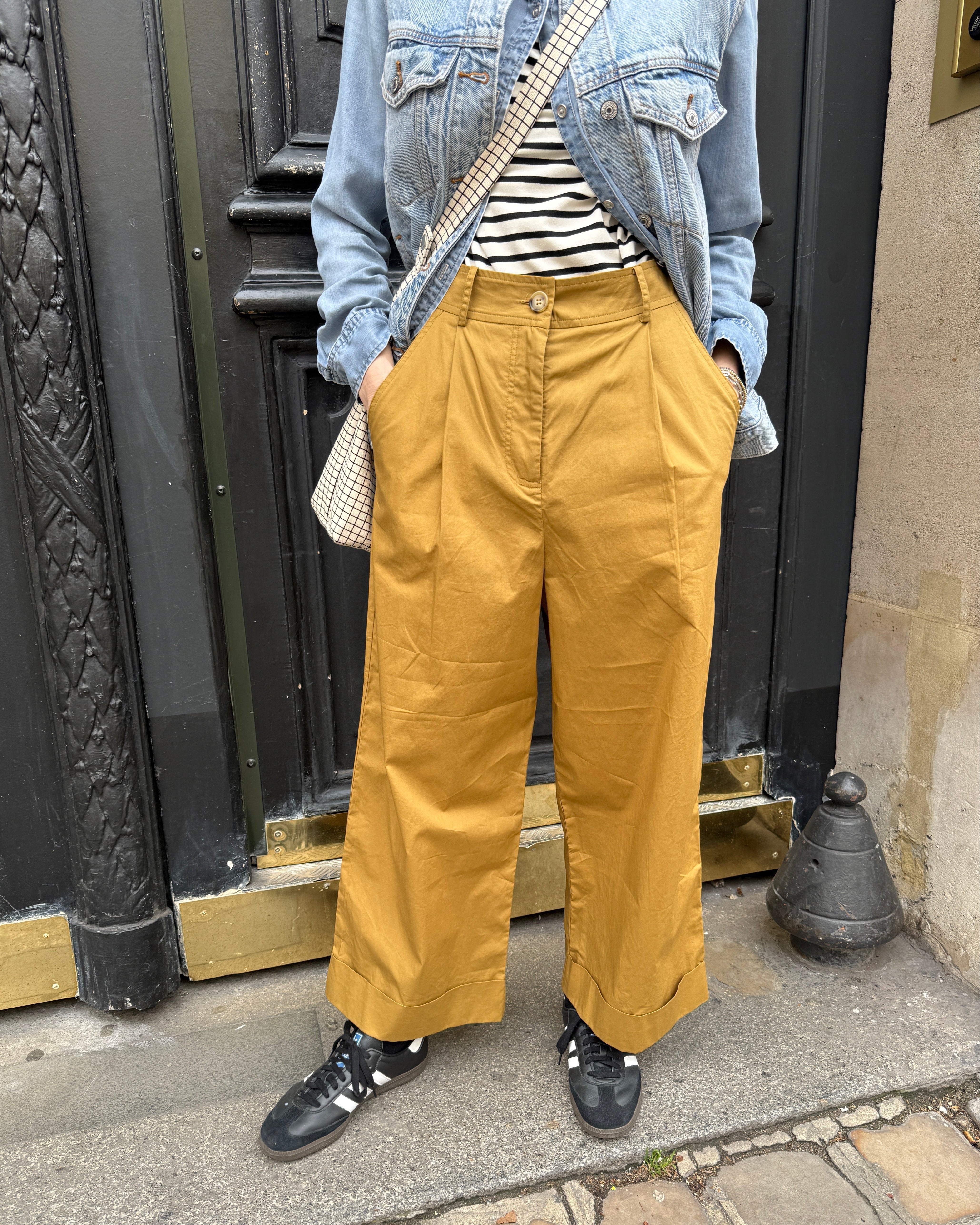 Woman wearing camel color pleated dress pants with wide leg and cuff with black and white striped shirt
