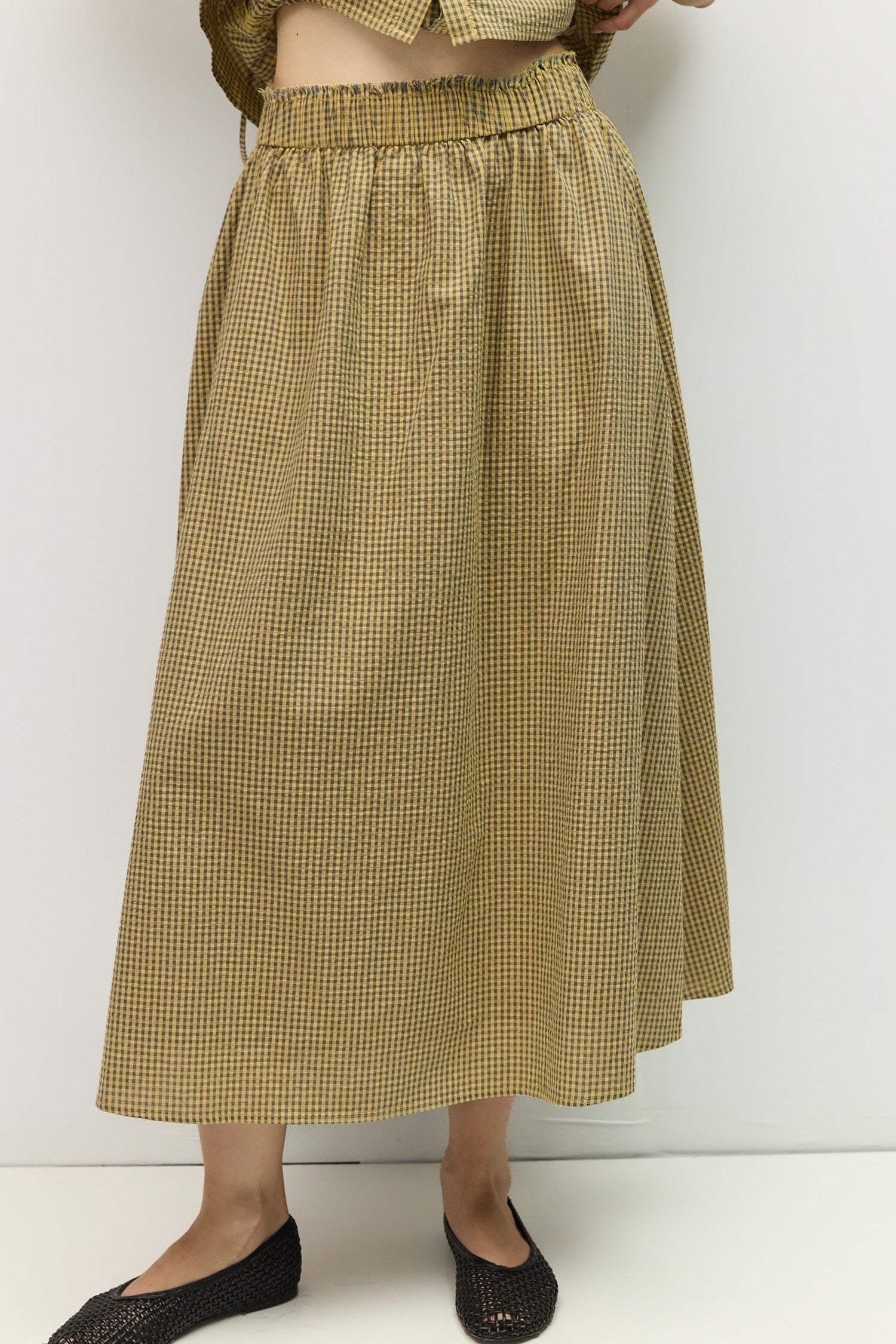 Person wearing a yellow checkered skirt against a white background