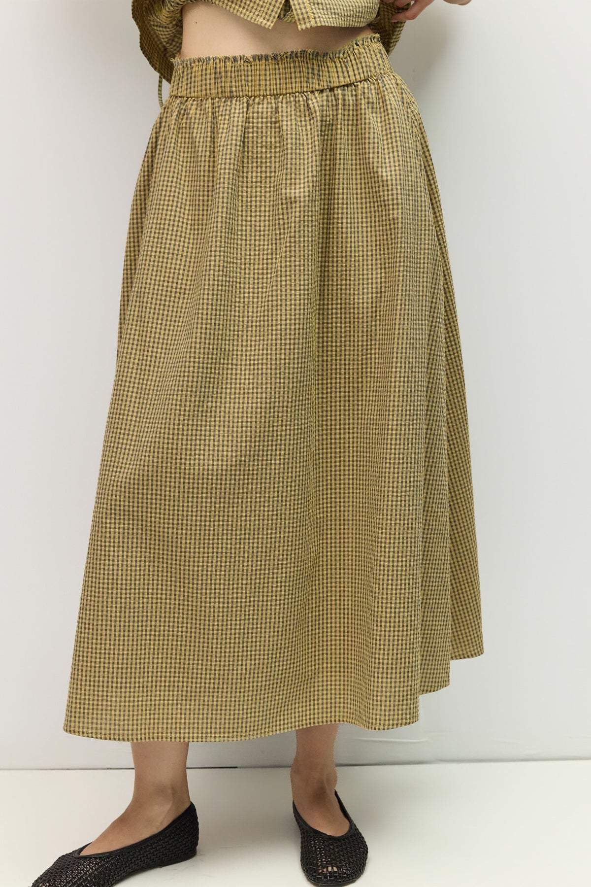 Person wearing a yellow checkered skirt against a white background