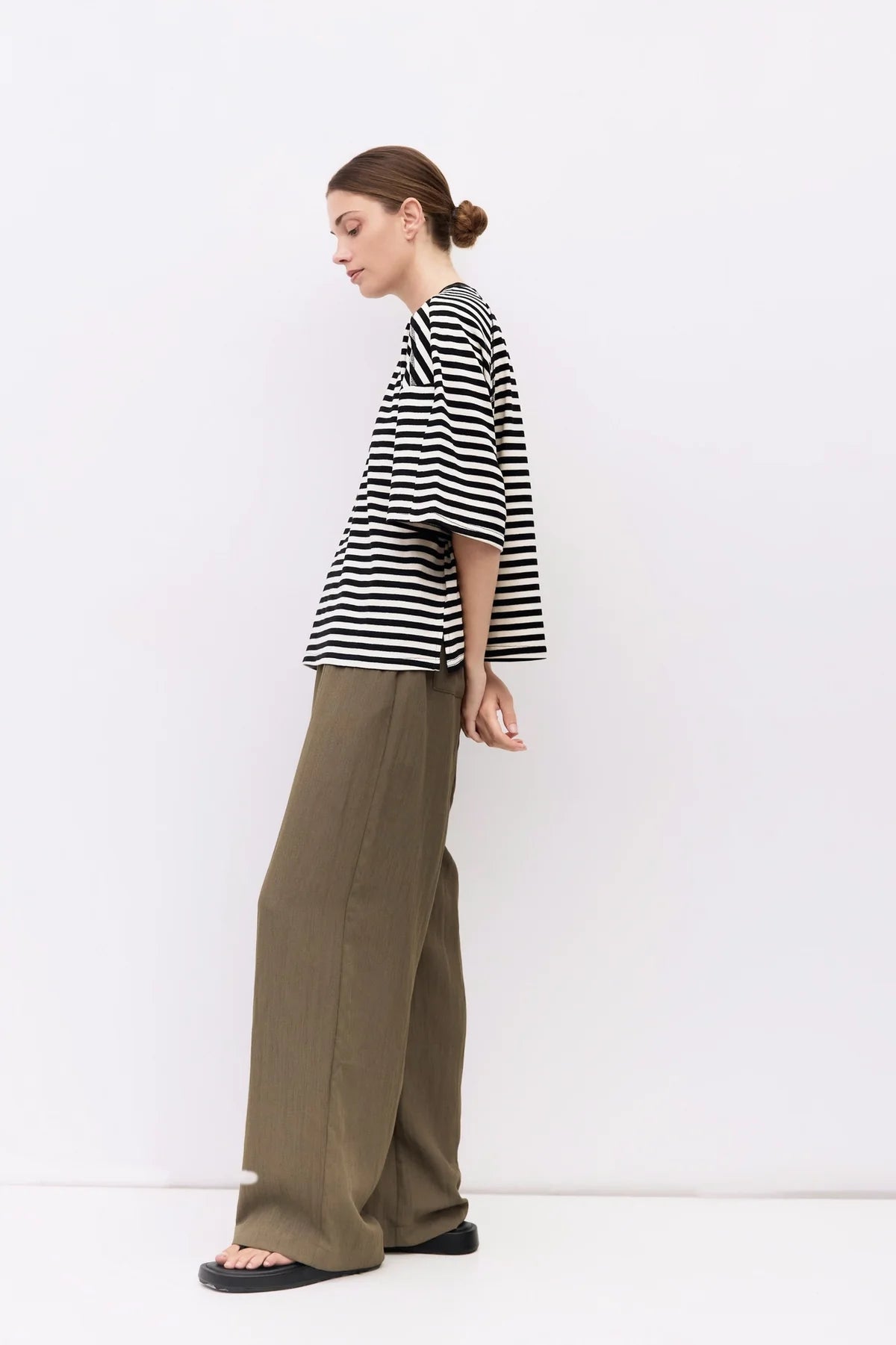 Woman wearing a black and white striped shirt and green pants against a white background