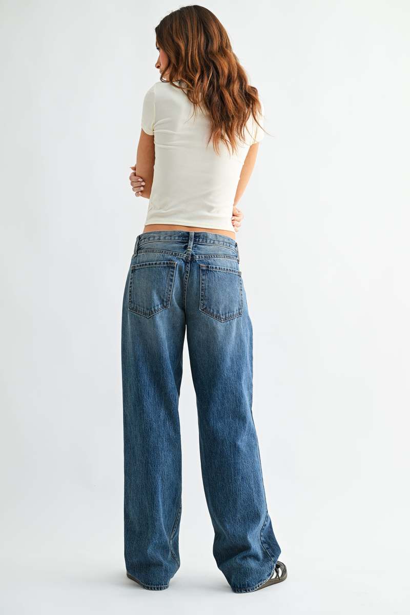 Person wearing blue jeans and a white top on a plain background