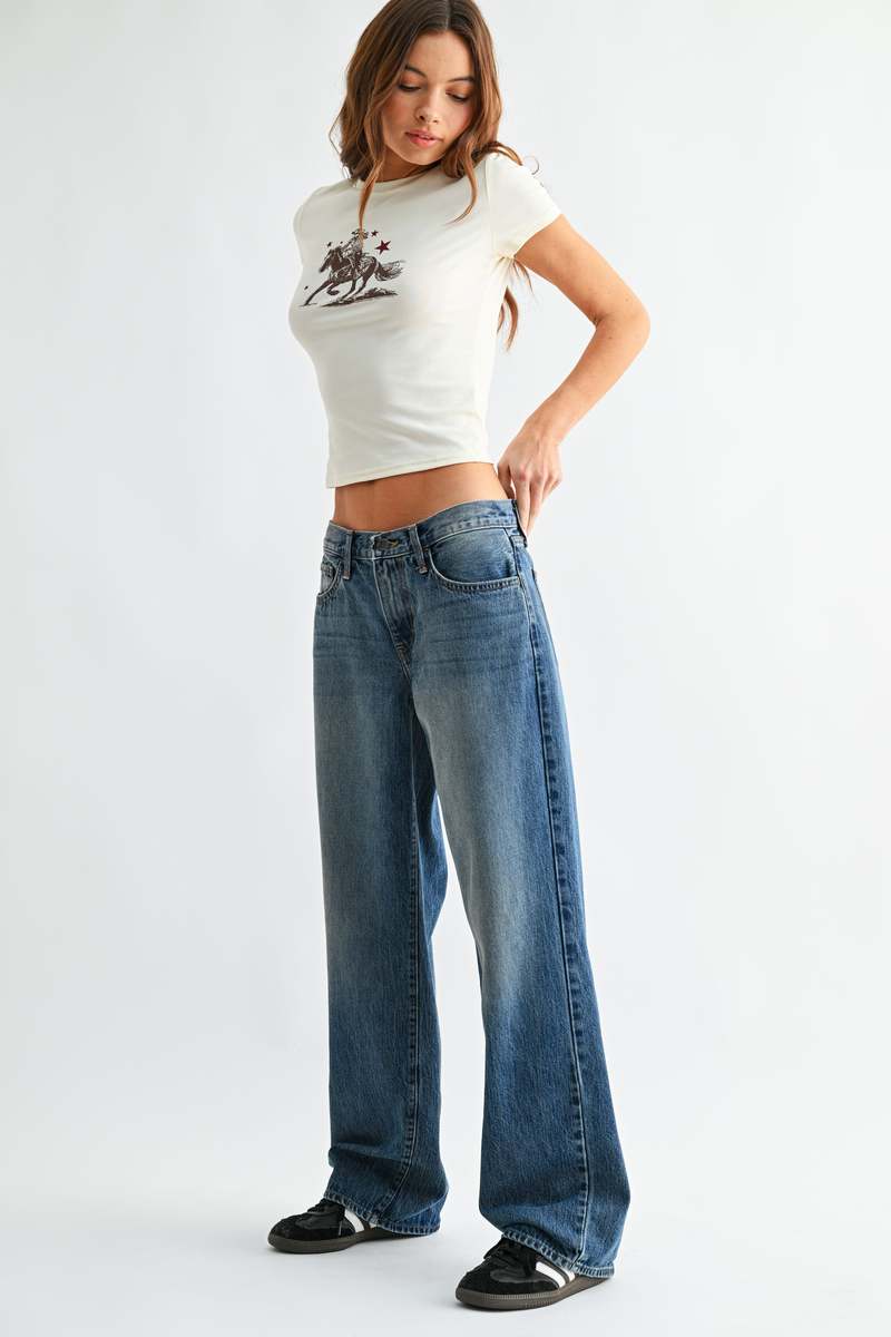 Woman wearing a white crop top with a graphic design and blue jeans on a white background