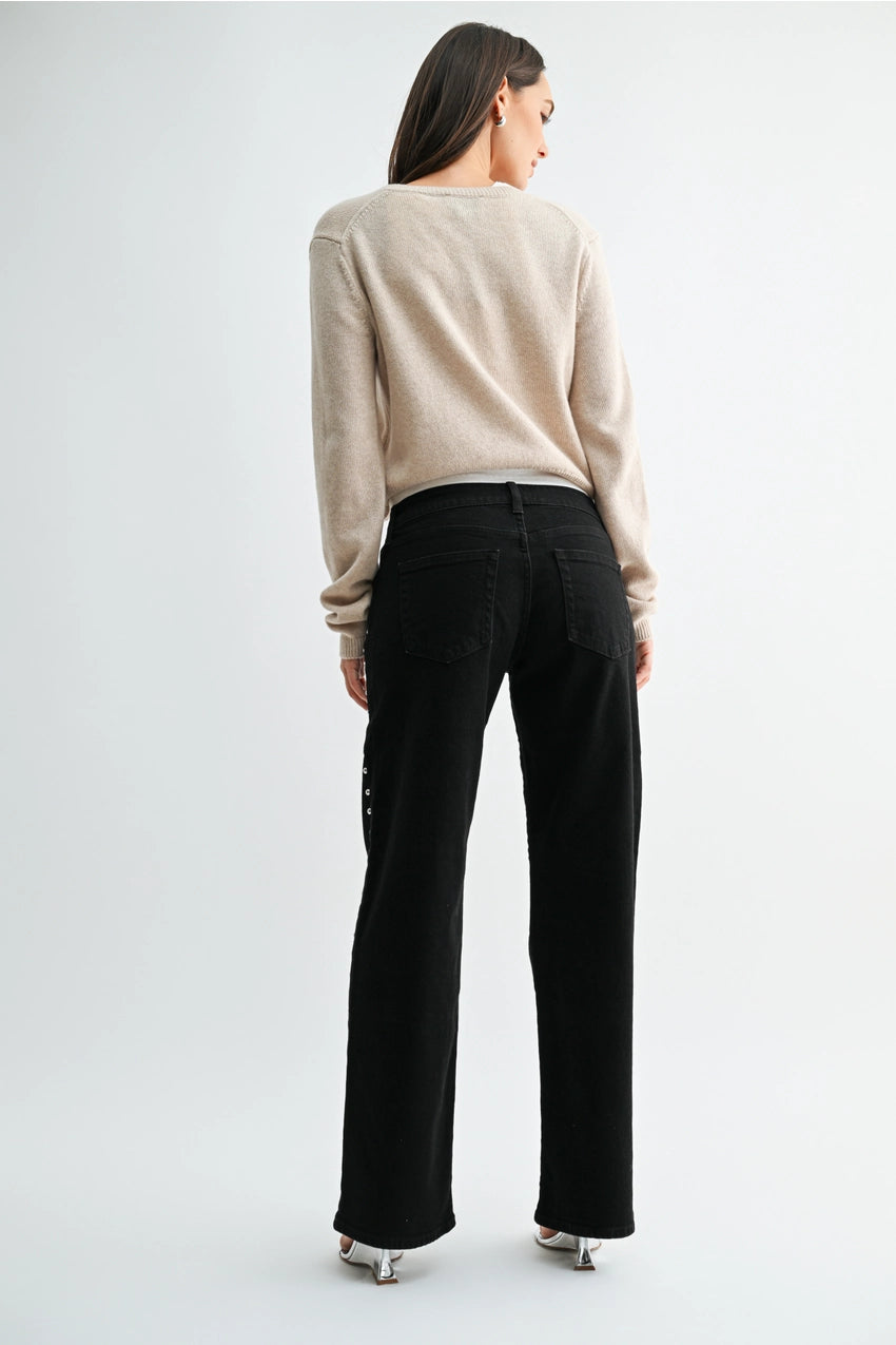 woman wearing black jeans and a cream sweater in front of a white background. 